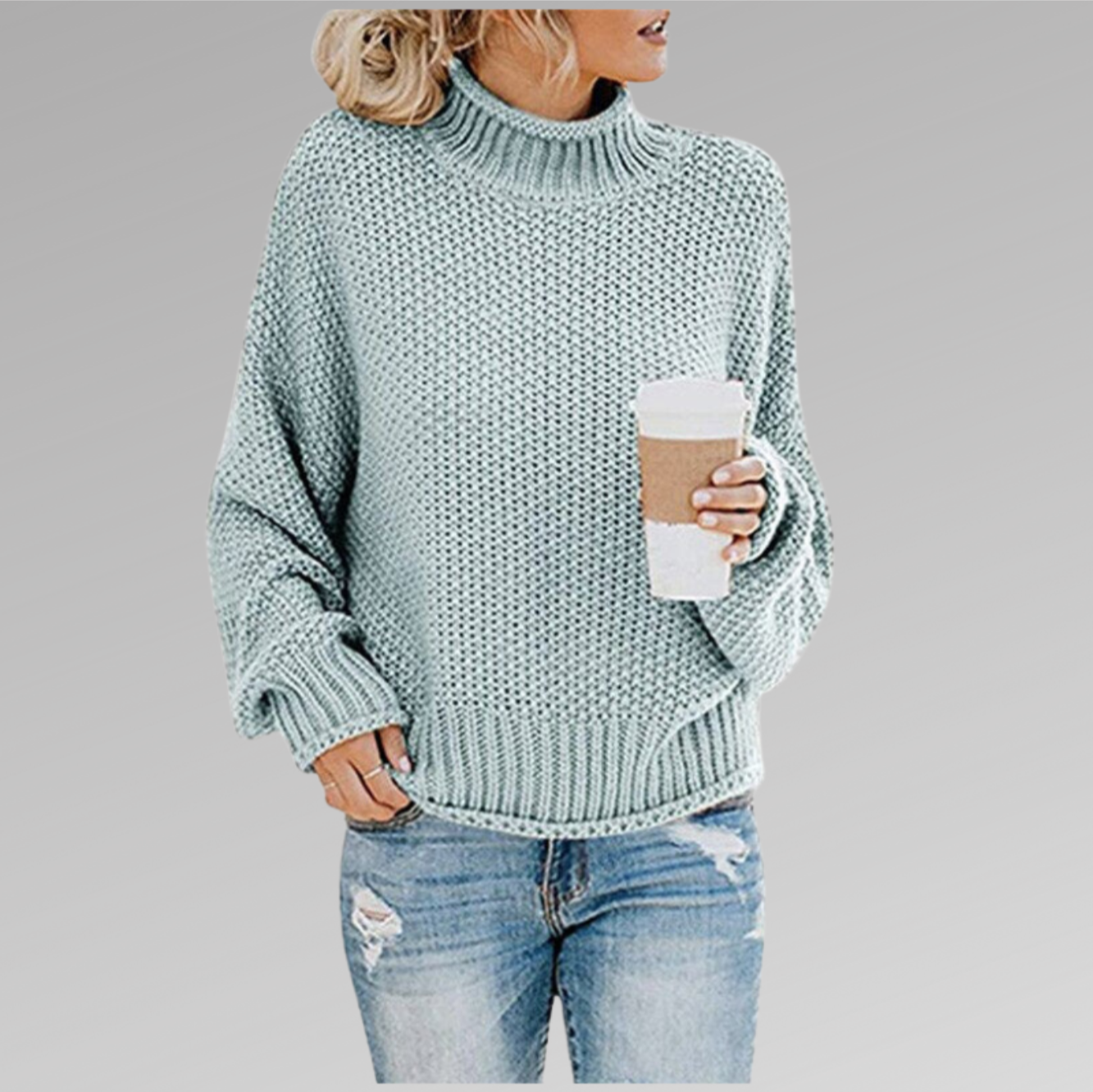 Femme portant un pull en maille vert menthe, tenant un gobelet de café, vêtue d'un jean déchiré. Mode décontractée automne-hiver.