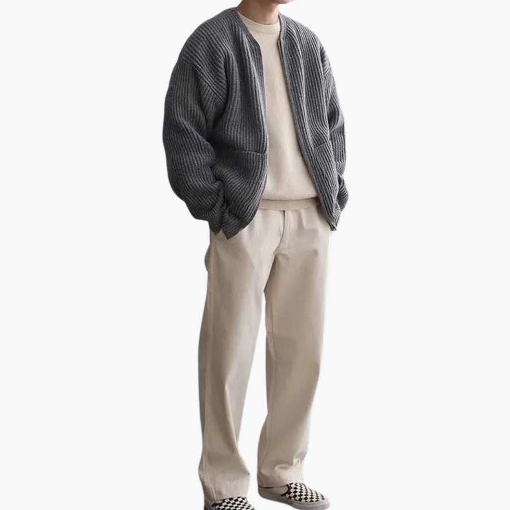 Homme portant un cardigan gris sur un pull beige, pantalon beige et chaussures à carreaux. Mode décontractée, tenue automne-hiver élégante.