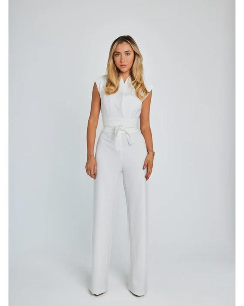 Femme en combinaison blanche élégante, posant debout sur fond blanc. Mode féminine, tenue chic, style moderne, vêtements tendance.