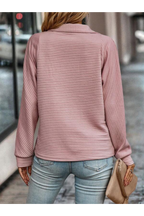 Femme en pull rose texturé, manches longues, tenant un sac beige, marchant en ville. Mode féminine, tenue décontractée, style urbain chic.