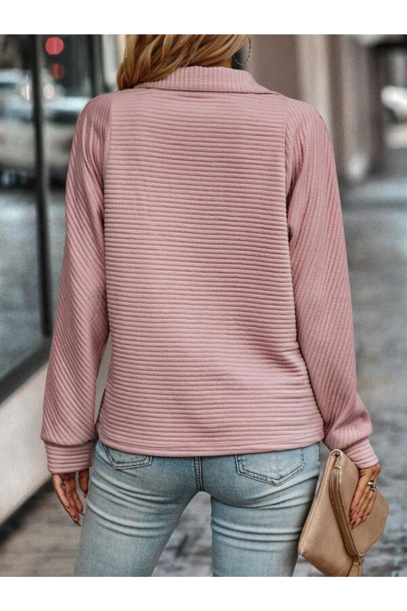 Femme en pull rose texturé, manches longues, tenant un sac beige, marchant en ville. Mode féminine, tenue décontractée, style urbain chic.