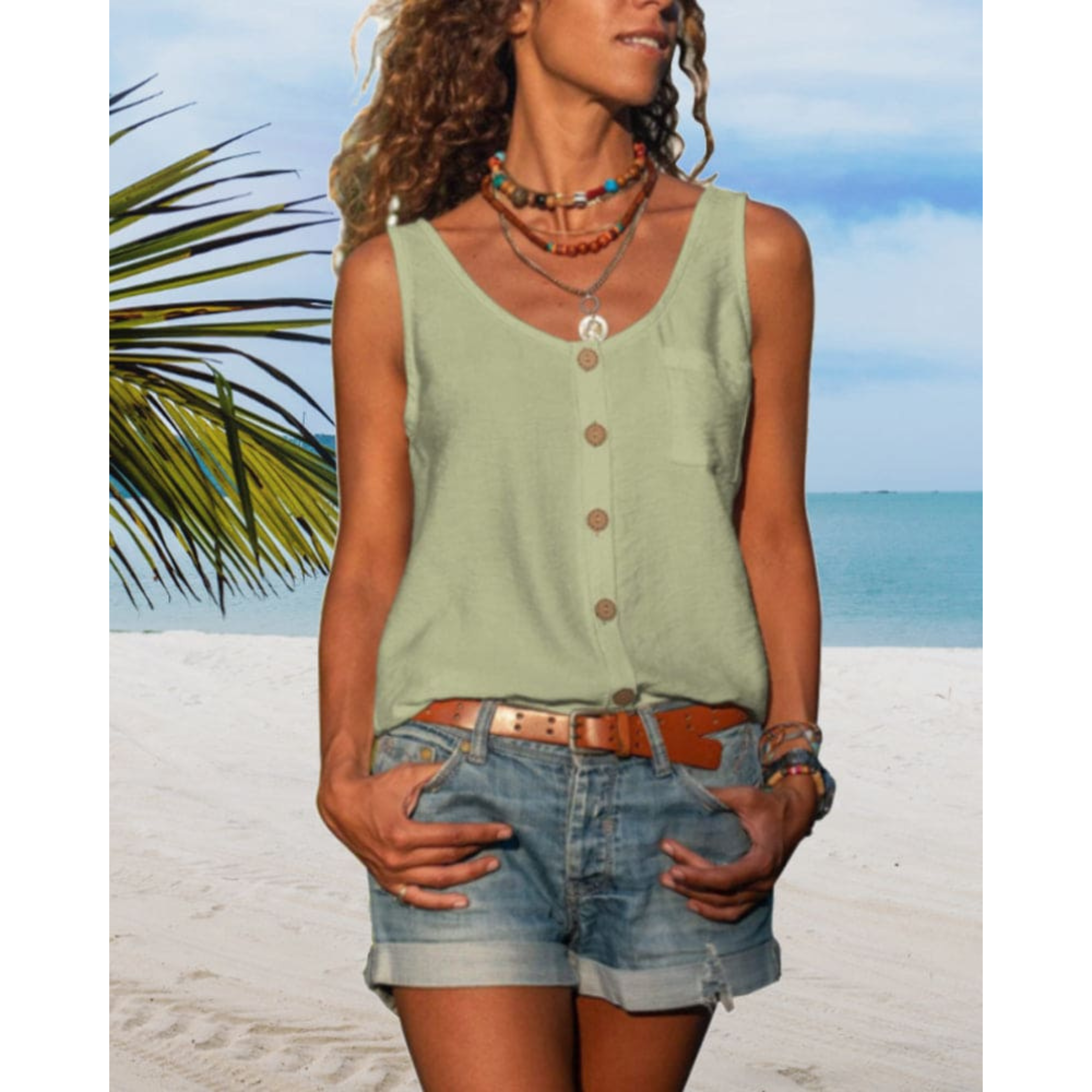 Femme en débardeur vert et short en jean sur plage tropicale, collier coloré, ciel bleu, mer en arrière-plan, ambiance estivale et décontractée.