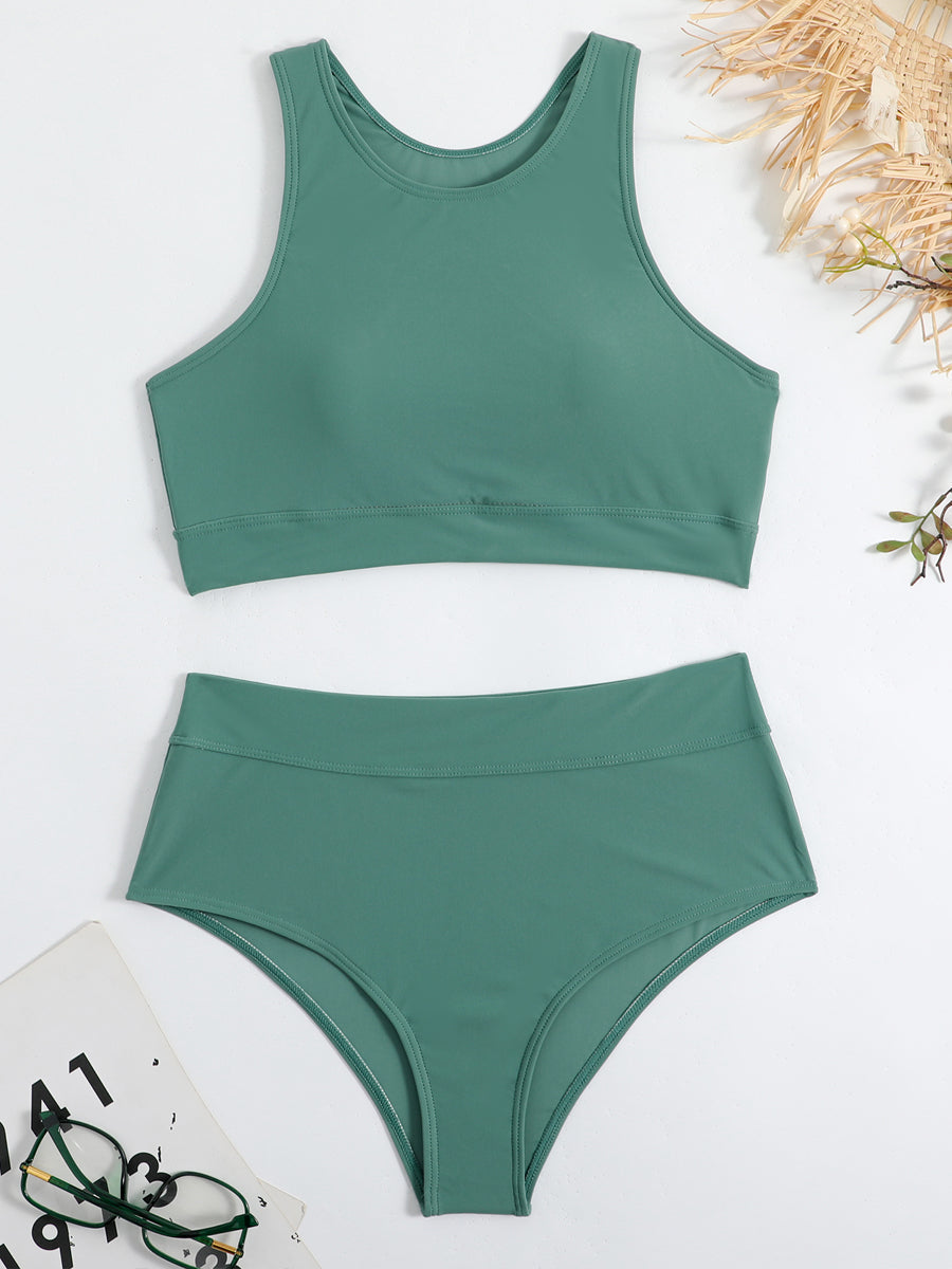 Maillot de bain deux pièces vert, haut à col rond et bas taille haute, posé sur fond blanc avec lunettes et chapeau en paille.