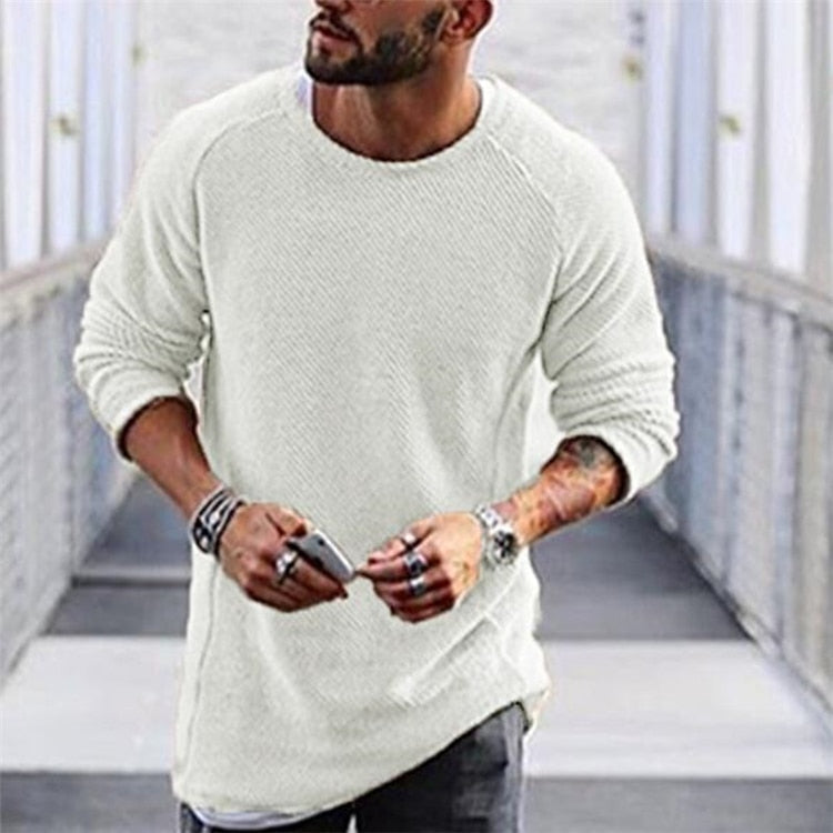 Homme portant un pull blanc en tricot, manches longues, posant dans un couloir moderne. Mode masculine, style décontracté, accessoires tendance.