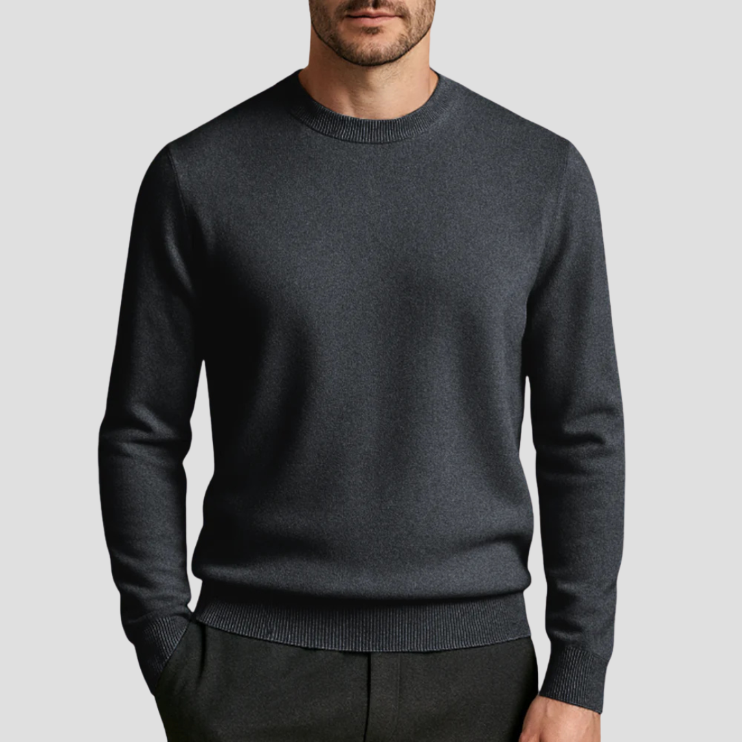 Homme portant un pull en laine mérinos gris foncé, col rond, manches longues, style élégant et moderne, sur fond gris clair. Mode masculine chic.