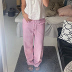Femme en pyjama rayé rose et blanc, debout dans une chambre moderne avec lit et coussins. Mode détente, confort à la maison.