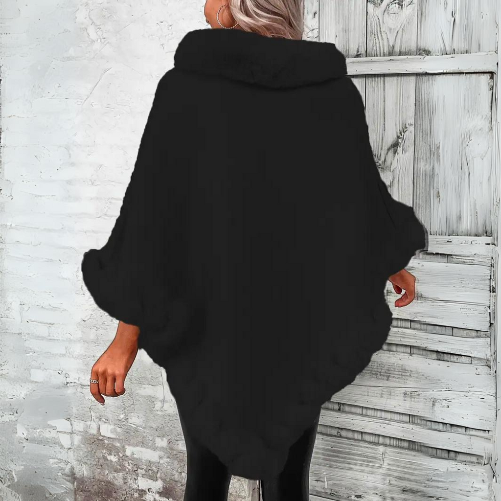 Femme portant un poncho noir élégant, devant une porte en bois vieilli. Mode automne-hiver, vêtement chaud et tendance.