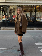Jeune femme en manteau marron et bottes en cuir devant le Café de Flore à Paris, style automnal chic, rue animée, ambiance parisienne.