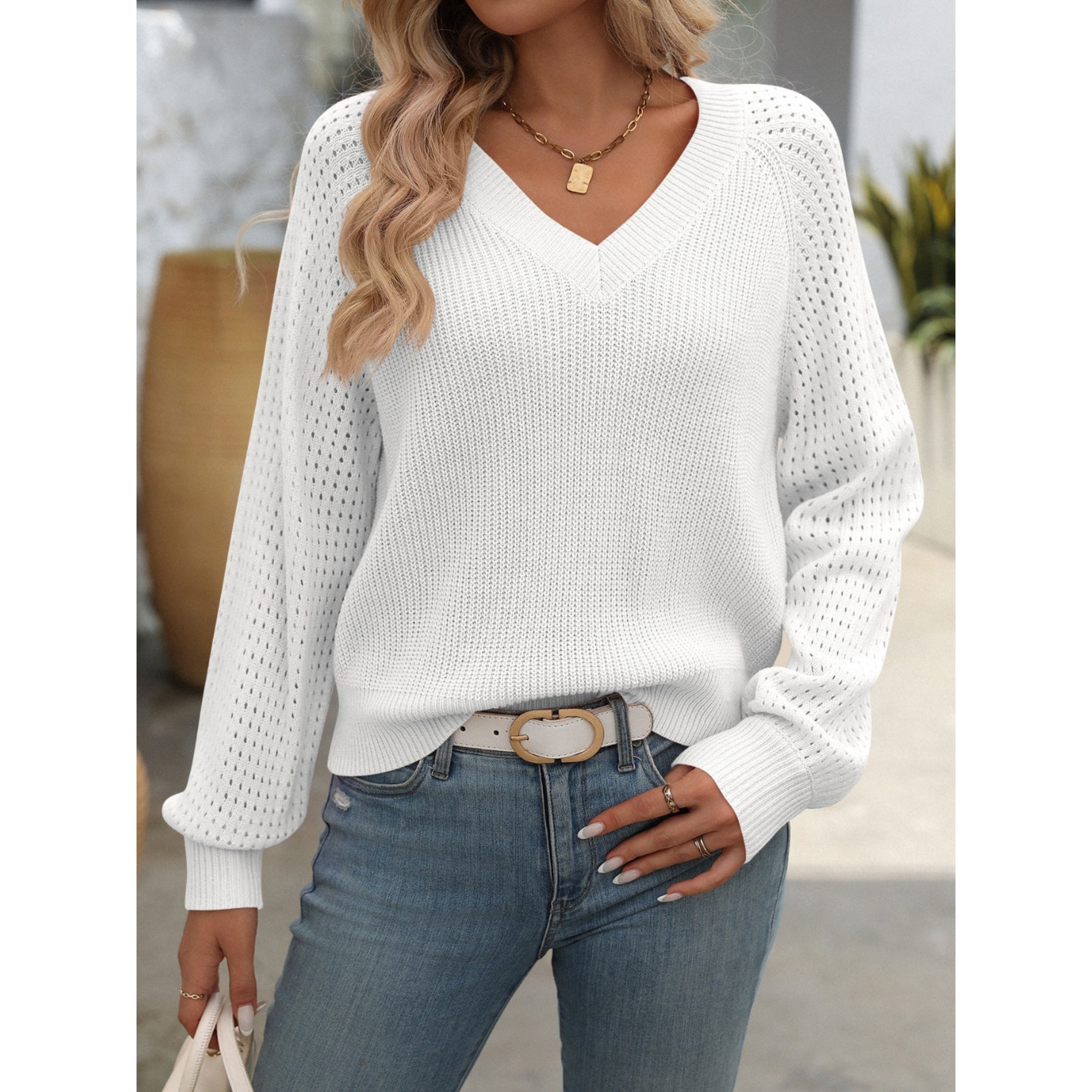 Femme portant un pull blanc à col en V, manches longues ajourées, avec un jean bleu. Style décontracté chic, idéal pour l'automne.