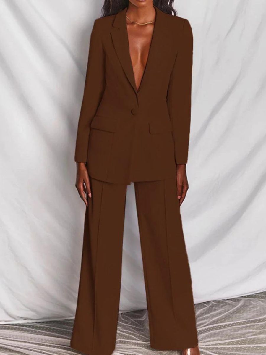 Femme portant un costume marron élégant, veste à col en V profond, pantalon large, sur fond blanc. Mode féminine, tenue professionnelle chic.