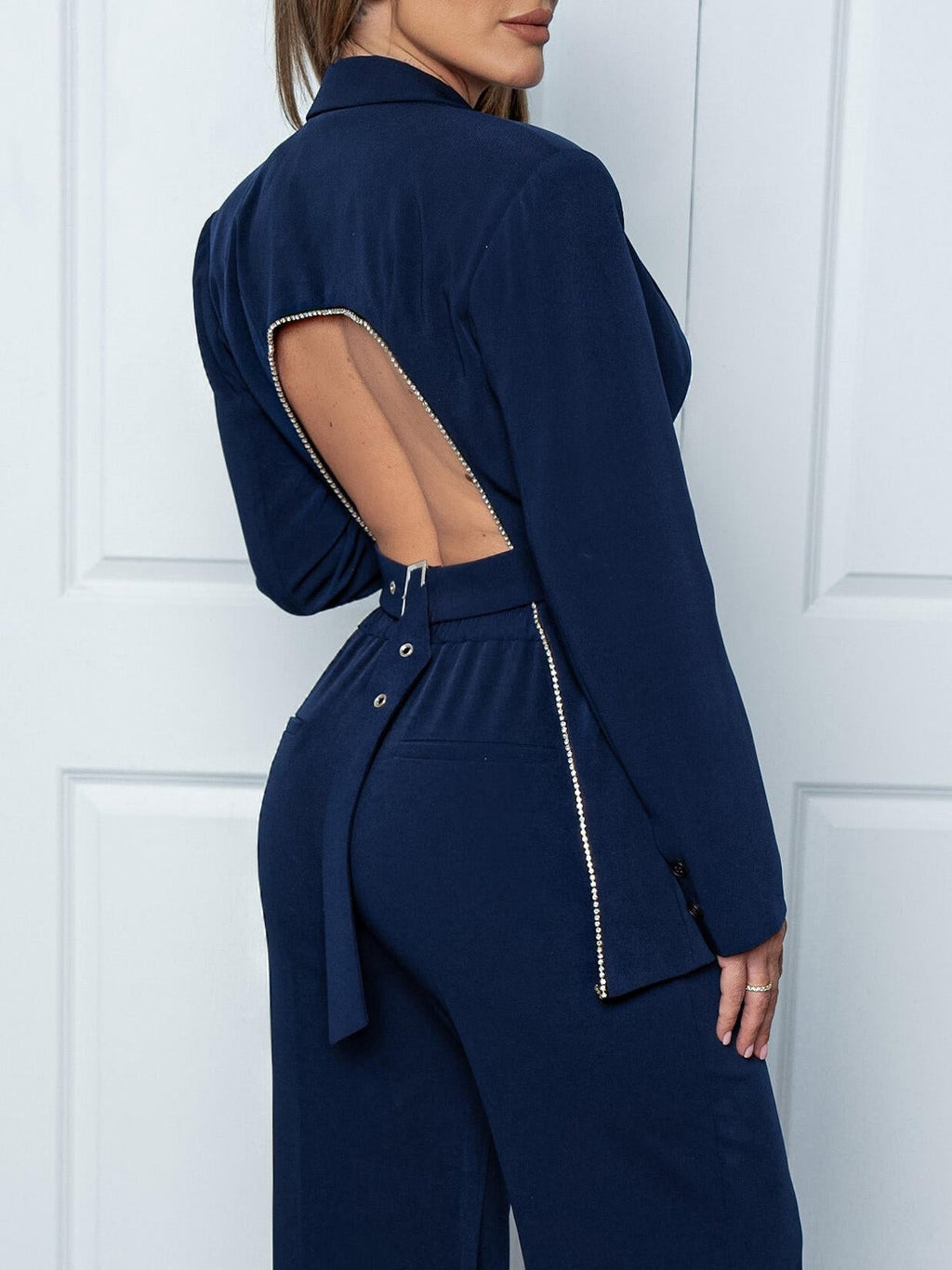 Femme portant une combinaison bleu marine élégante avec dos ouvert et détails zippés, mode tendance, tenue chic pour soirée ou événement spécial.