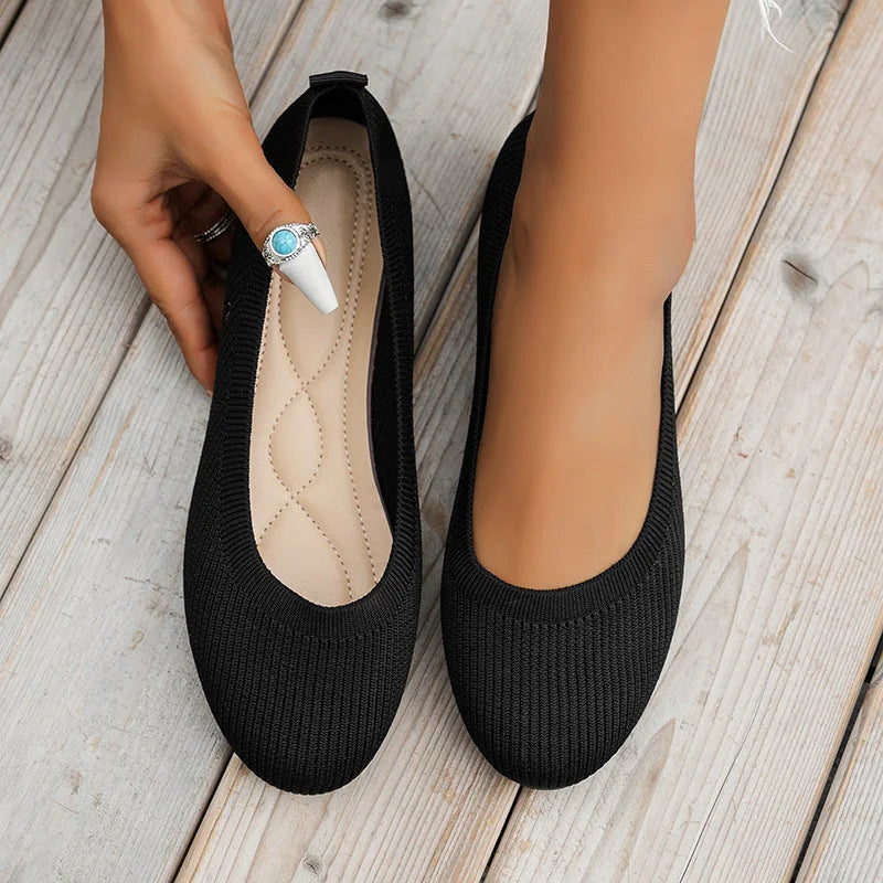 Ballerines noires élégantes sur fond de bois clair, main féminine ajustant une chaussure. Chaussures confortables, mode féminine, style décontracté.