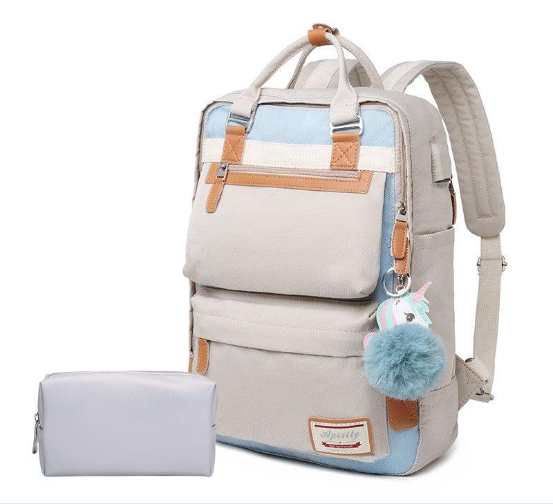Sac à dos beige et bleu avec pompon bleu et porte-clés licorne, accompagné d'une trousse grise. Design moderne, idéal pour école ou voyage.
