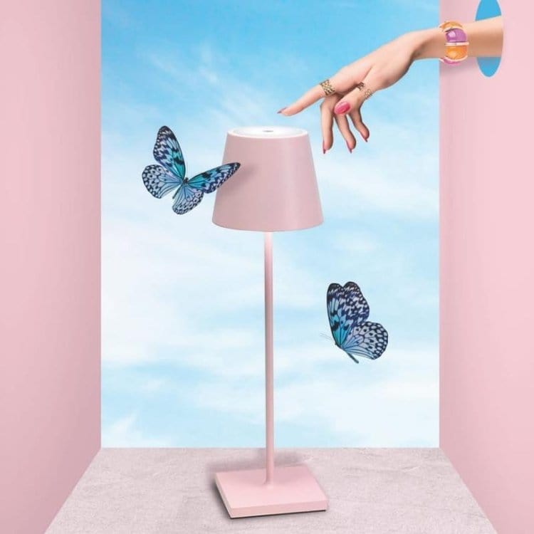 Lampe rose moderne avec papillons bleus, main féminine avec bijoux, fond ciel bleu. Décoration intérieure élégante et tendance.