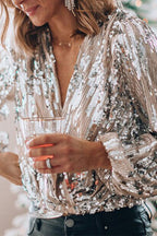 Femme portant un haut à paillettes argentées, tenant un verre. Mode festive, tenue élégante, soirée glamour. Accessoires brillants, style chic.