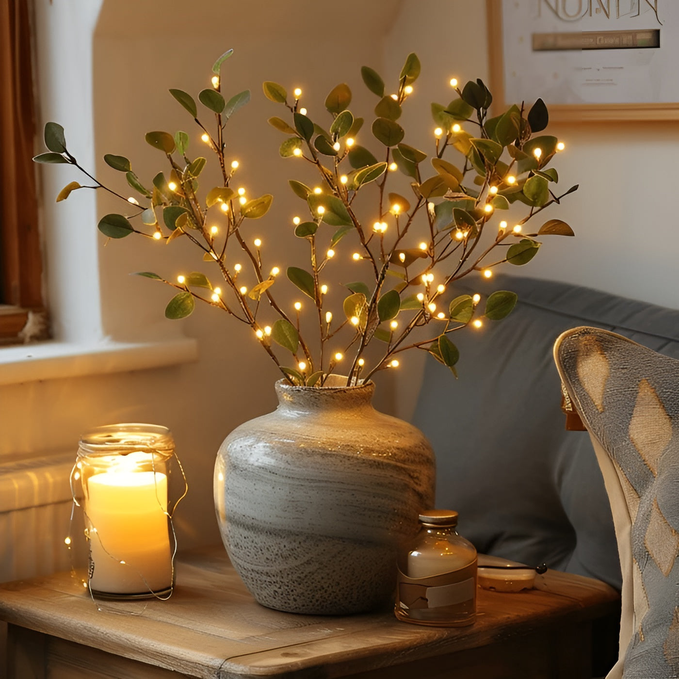 Vase en céramique avec branches lumineuses LED, posé sur une table en bois à côté d'une bougie allumée, créant une ambiance chaleureuse et cosy.