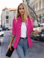 Femme élégante en veste rose vif avec boutons argentés, manches à motif léopard, tenant un smartphone et une pochette noire, marchant en ville.