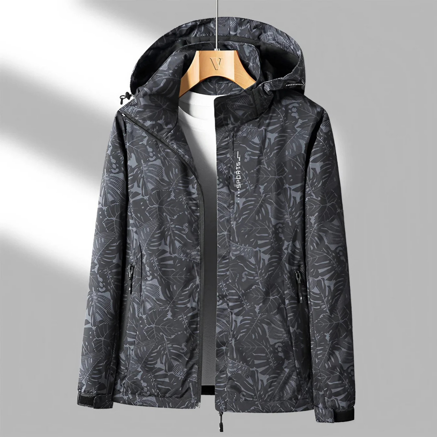 Veste imperméable à capuche pour homme, motif camouflage gris, accrochée sur cintre en bois, idéale pour randonnée et activités extérieures.