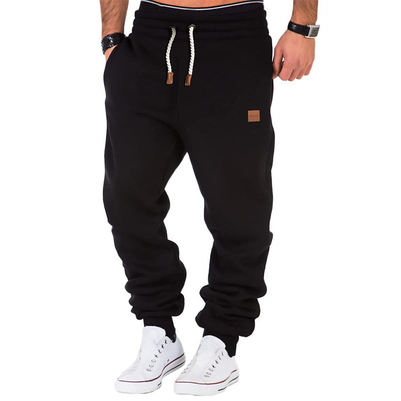 Pantalon de jogging noir pour homme avec cordon de serrage, poches latérales, porté avec des baskets blanches. Mode décontractée masculine.