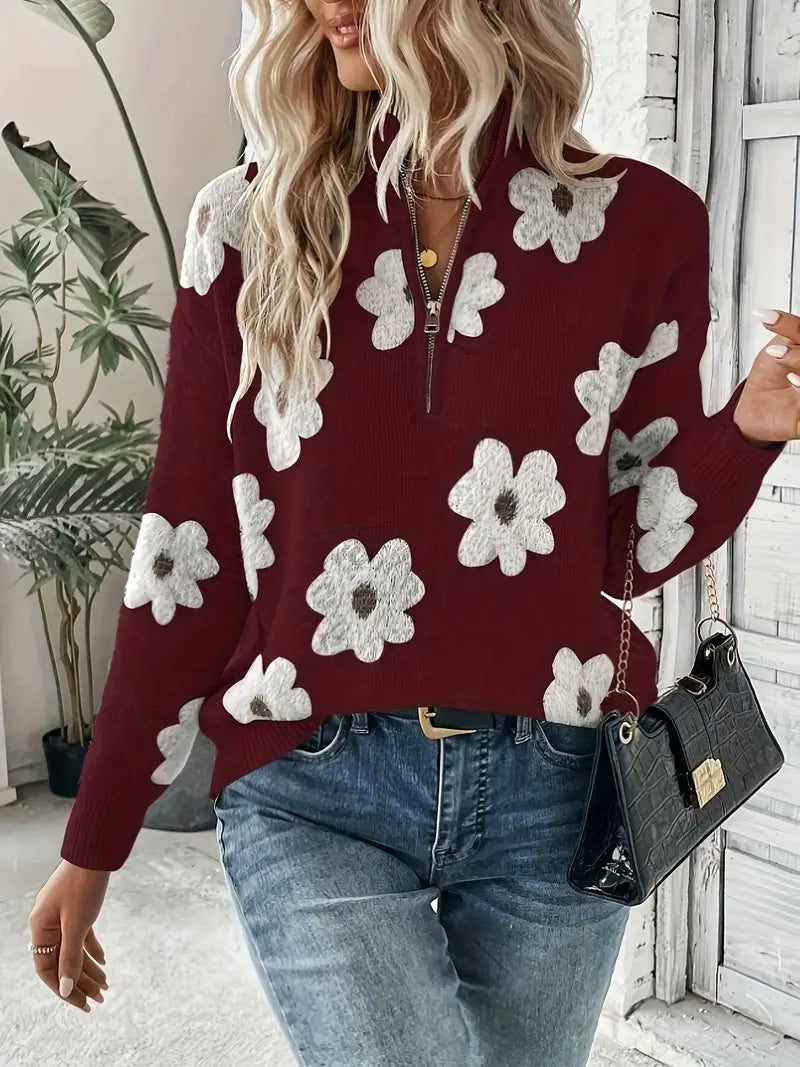 Femme portant un pull rouge à fleurs blanches, jean bleu et sac à main noir. Mode automne, style décontracté, tendance féminine.