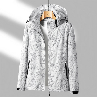 Veste imperméable à capuche, motif feuillage blanc et gris, accrochée sur un cintre en bois. Mode femme, vêtement extérieur tendance.