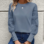 Femme portant un chemisier bleu à manches longues avec motifs floraux, col rond, boutons aux poignets, associé à un jean. Mode élégante et décontractée.