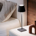 Lampe de chevet moderne noire sur table de nuit blanche, à côté d'un lit avec oreiller gris, éclairage d'intérieur élégant et minimaliste.