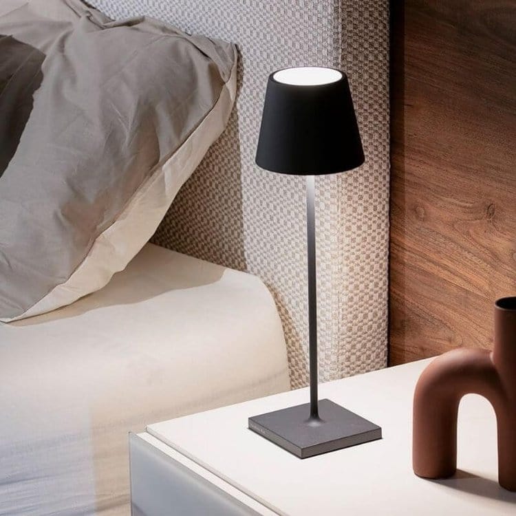 Lampe de chevet moderne noire sur table de nuit blanche, à côté d'un lit avec oreiller gris, éclairage d'intérieur élégant et minimaliste.