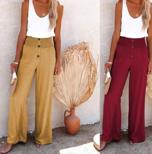 Femme en débardeur blanc et pantalon large taille haute, beige à gauche, bordeaux à droite, tenant une pochette beige, devant un mur blanc et vase décoratif.