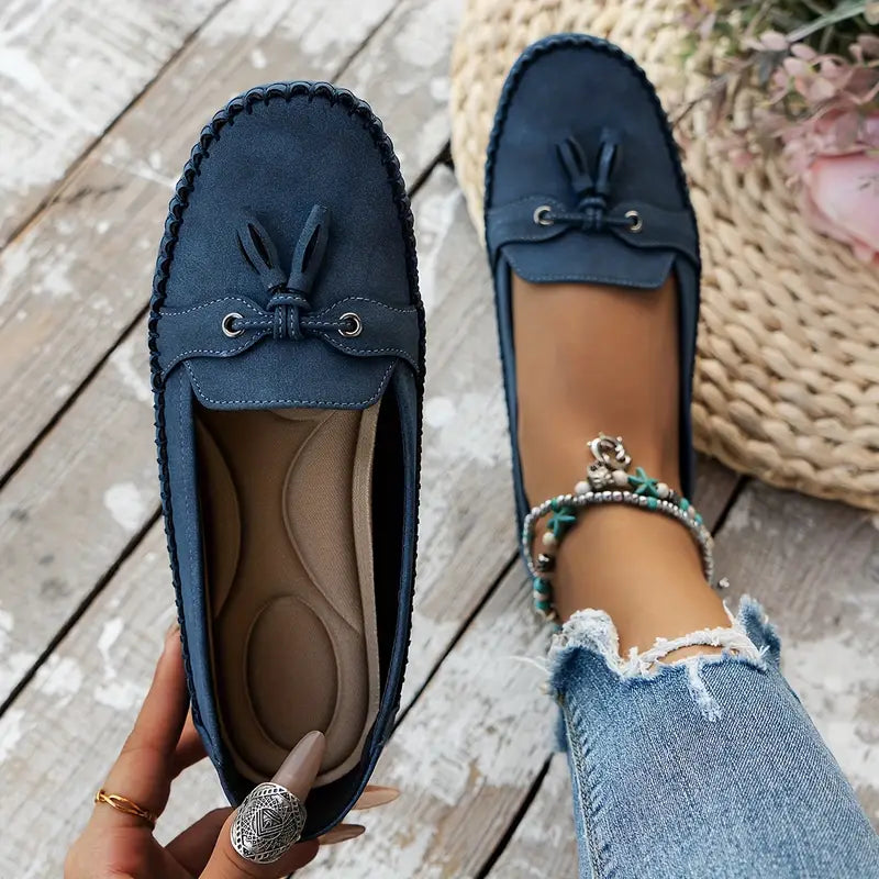 Mocassins bleus en daim pour femme avec lacets, portés avec un jean déchiré. Chaussures confortables et élégantes sur fond de bois clair.