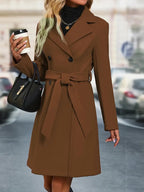 Femme en manteau marron élégant, tenant un café et un sac à main noir, marchant en ville. Mode automne, style urbain chic, tendance féminine.