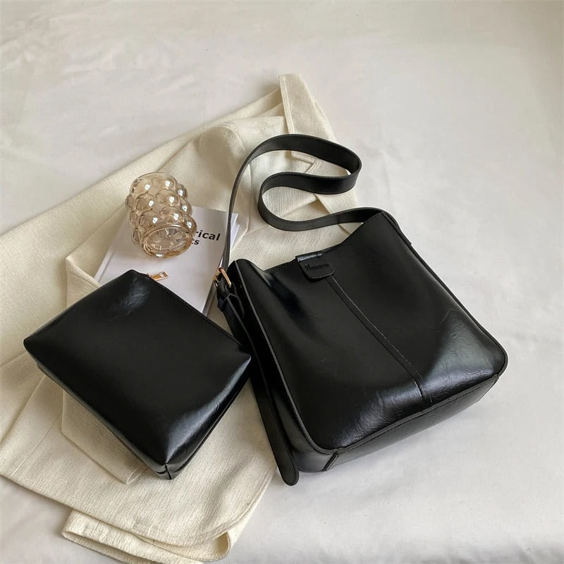 Sac à main en cuir noir élégant avec pochette assortie sur fond blanc, accessoire mode femme, design moderne, idéal pour tenue chic et tendance.