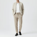 Homme portant un ensemble décontracté beige, composé d'un cardigan et d'un pantalon en maille, avec des baskets noires. Mode masculine élégante.
