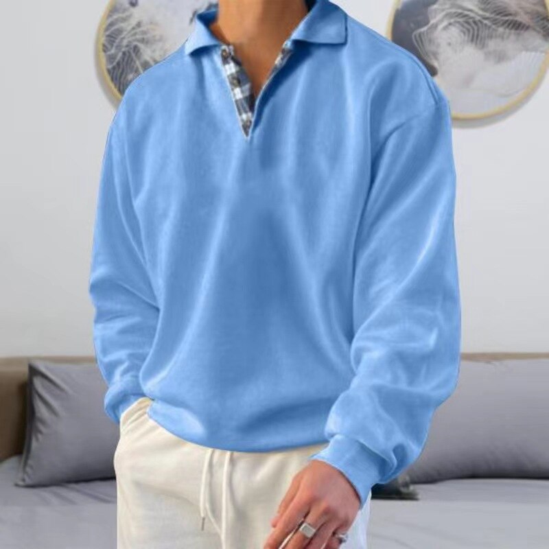 Homme portant un pull bleu clair à col en V avec chemise à carreaux, debout dans un salon moderne. Mode masculine, tenue décontractée élégante.