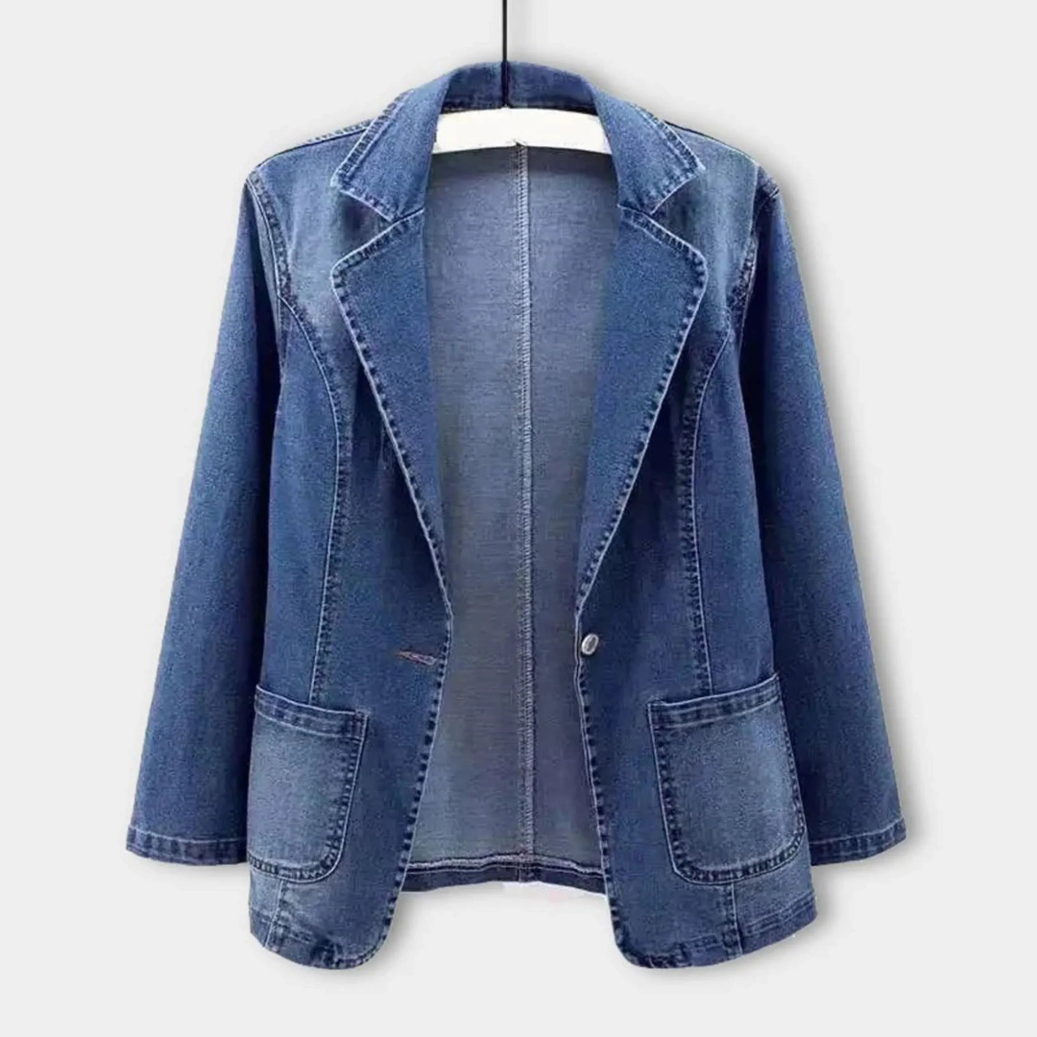 Veste en jean bleu pour femme, style blazer, avec poches avant, suspendue sur un cintre. Mode décontractée, tendance automne-hiver.