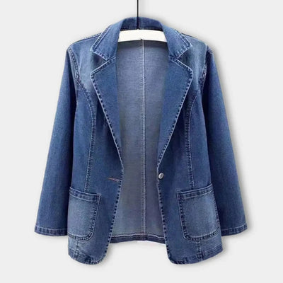 Veste en jean bleu pour femme, style blazer, avec poches avant, suspendue sur un cintre. Mode décontractée, tendance automne-hiver.