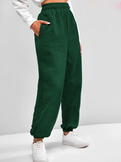 Pantalon de jogging vert foncé pour femme, taille haute, avec poches, porté avec des baskets blanches. Mode décontractée et confortable.