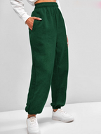 Pantalon de jogging vert foncé pour femme, taille haute, avec poches, porté avec des baskets blanches. Mode décontractée et confortable.