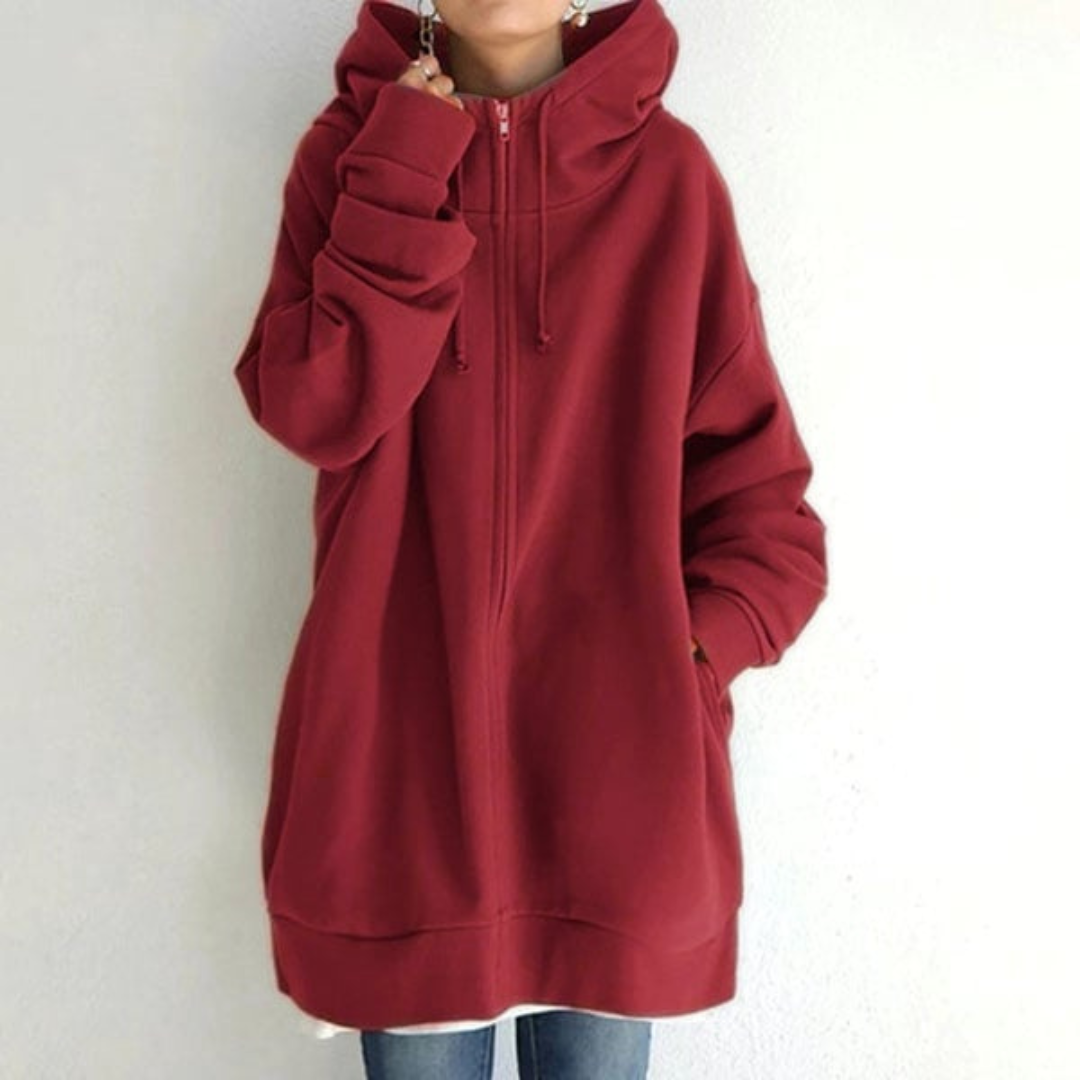 Sweat à capuche rouge oversize, manches longues, fermeture éclair, porté par une personne debout, style décontracté, tendance automne-hiver.