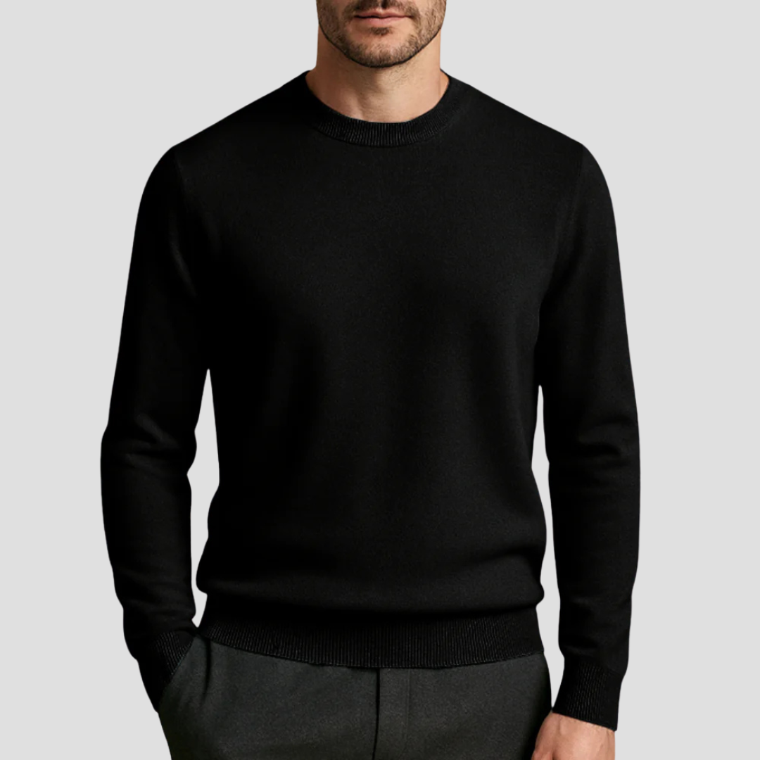 Homme portant un pull noir élégant, col rond, manches longues, sur fond gris. Mode masculine, vêtement chic, style automne-hiver.
