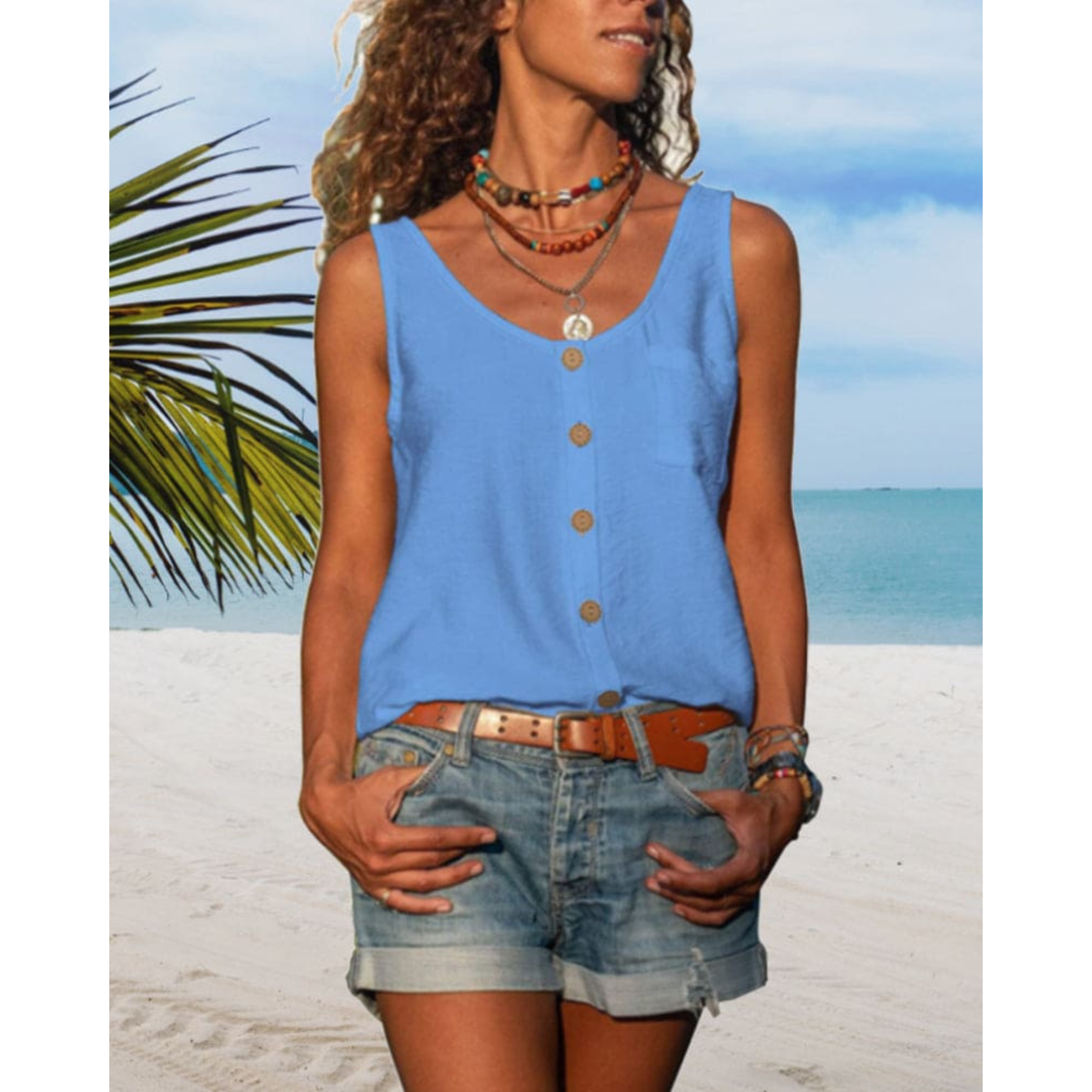 Femme en débardeur bleu et short en jean sur plage tropicale, collier coloré, ciel bleu, mer en arrière-plan, vacances d'été, mode décontractée.