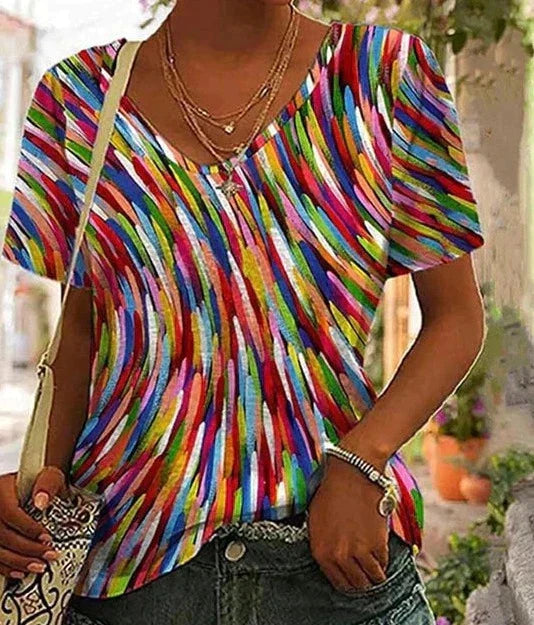 Femme portant un t-shirt coloré à motifs abstraits, col en V, manches courtes, avec un collier doré et un sac à main. Mode estivale tendance.