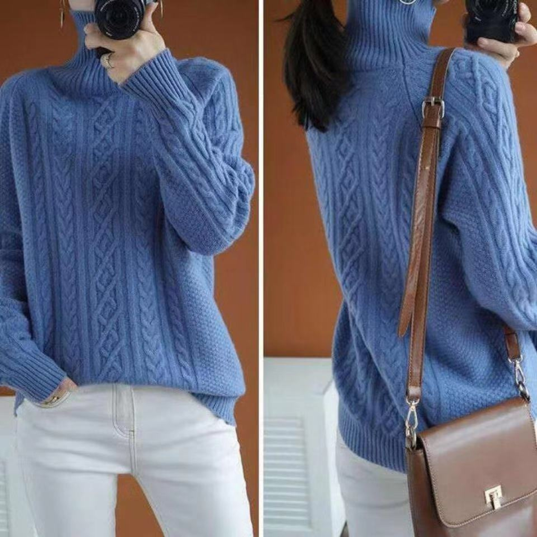 Femme portant un pull bleu en maille torsadée avec col roulé, associé à un sac à bandoulière marron et un pantalon blanc. Mode automne-hiver.