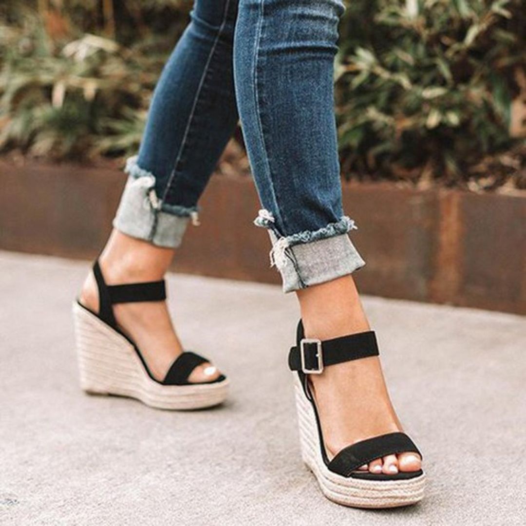Jeans ajustés et sandales compensées noires avec semelles en corde, portées en extérieur. Mode féminine, chaussures tendance, style décontracté.