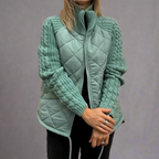 Femme portant une veste matelassée verte avec manches en tricot, fermeture éclair, posant les bras croisés. Mode automne-hiver, style décontracté.