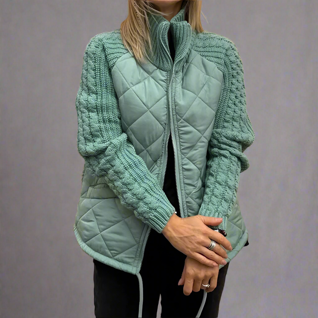 Femme portant une veste matelassée verte avec manches en tricot, fermeture éclair, posant les bras croisés. Mode automne-hiver, style décontracté.