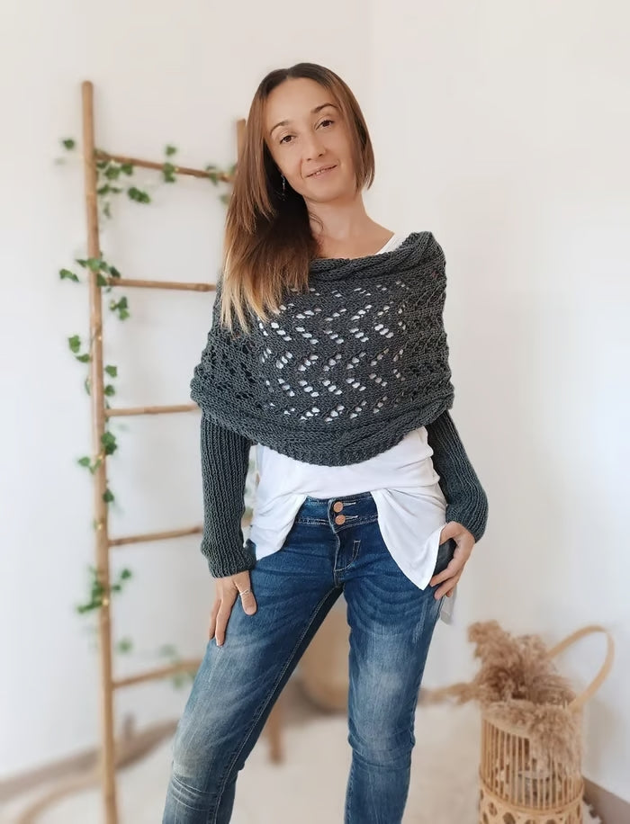 Dame portant un pull tricoté gris, posant devant une échelle en bois décorée de plantes. Mode automne, style décontracté, intérieur moderne.