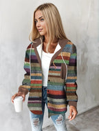 Femme blonde portant un cardigan multicolore à rayures, tenant un gobelet blanc. Mode automne, style décontracté, jeans déchirés.