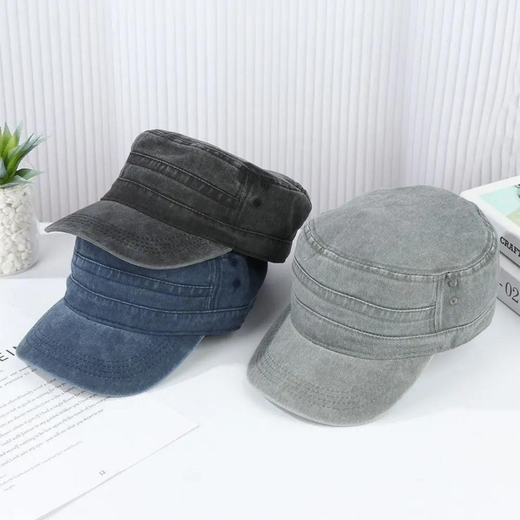 Trois casquettes militaires en denim gris, bleu et noir posées sur une table blanche, avec une plante verte en arrière-plan. Accessoires mode tendance.