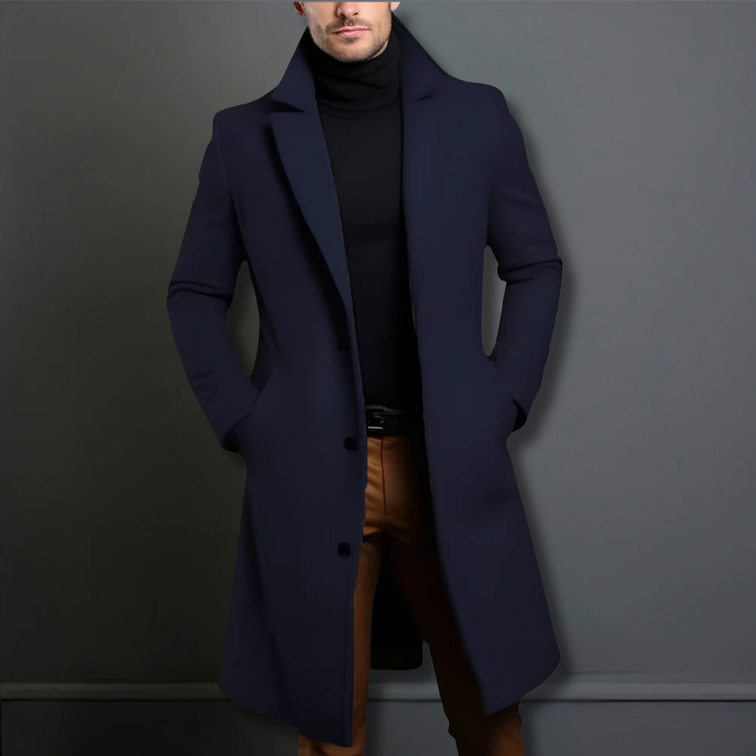Homme portant un manteau bleu marine élégant, col relevé, sur un pull noir et un pantalon marron. Mode masculine chic et moderne.